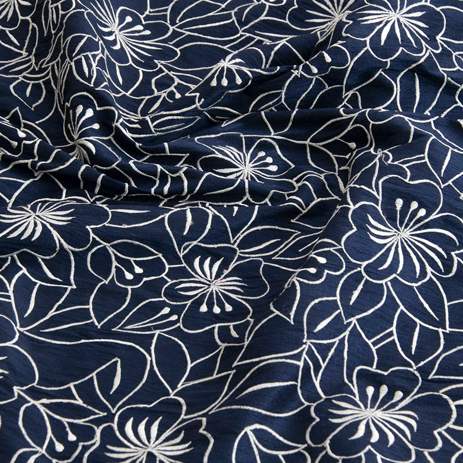 Wrinkled navy embroidery silk fabric with white floral motifs over a navy background, ideal for statement party looks or even luxurious homeware